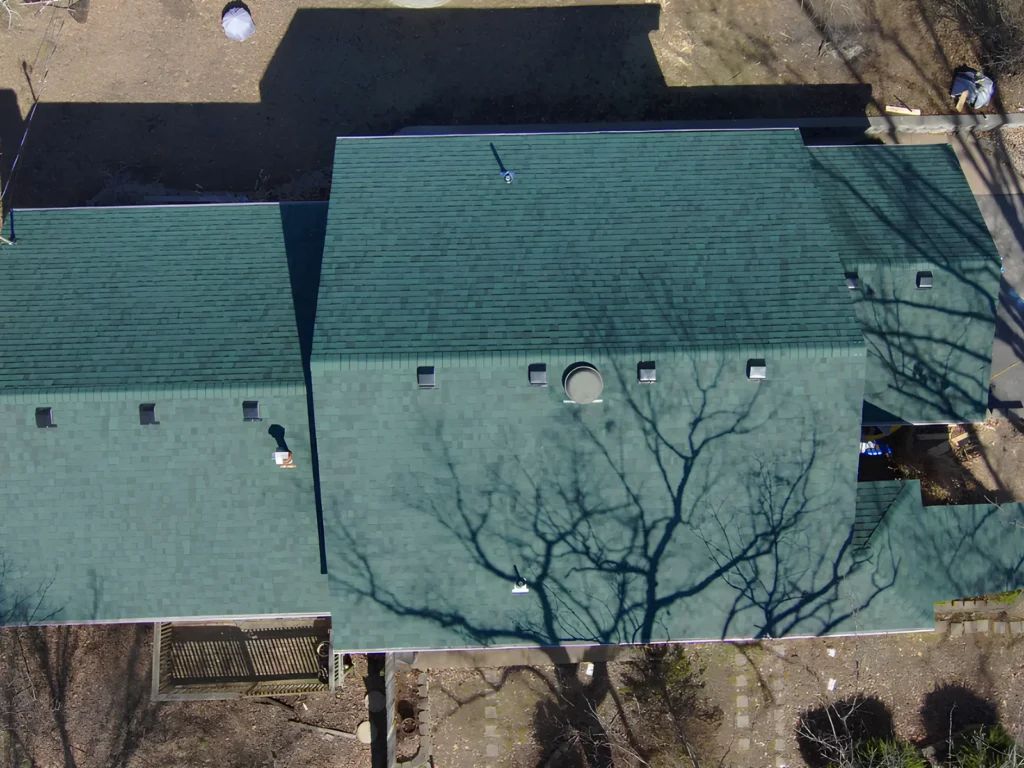 This image is showing a professionally installed green asphalt shingle roof on a residential property in Lake of the Ozarks, captured from an aerial drone perspective, highlighting the quality roofing workmanship and uniform installation.