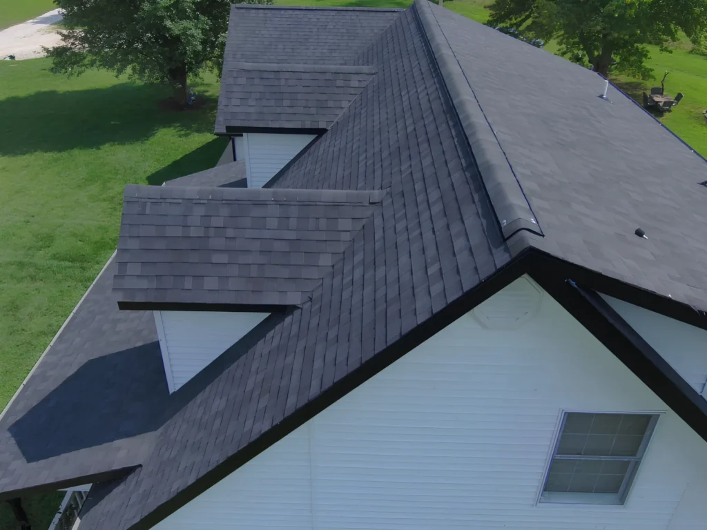 This image is showing a charcoal gray shingle roof installation on a white residential home in Lake Ozark, featuring multiple roof planes and precise ridge cap detail.