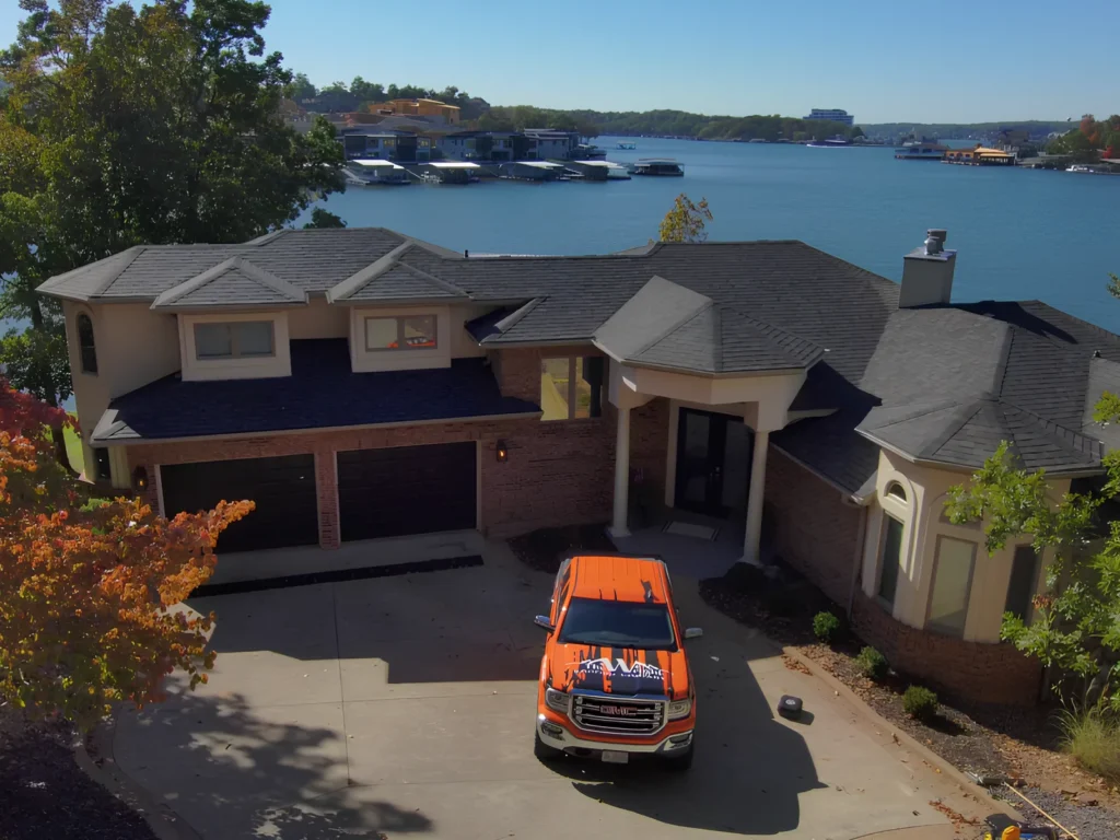 This image is showing a waterfront home with new roof installation, company service truck in driveway, and beautiful Lake Ozark views in the background.