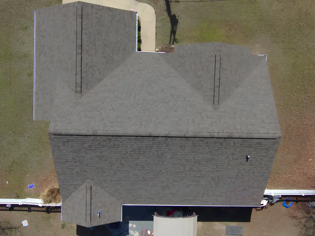This image is showing a top-down aerial view of a residential home with a newly installed gray architectural shingle roof featuring clean ridge lines and proper ventilation in Lake Ozark.