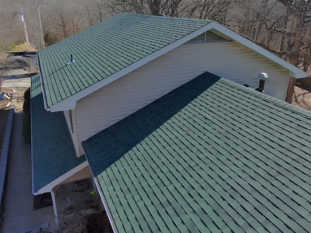 This image is showing a newly installed green architectural shingle roof with darker ridge caps on a white residential home near Lake of the Ozarks.