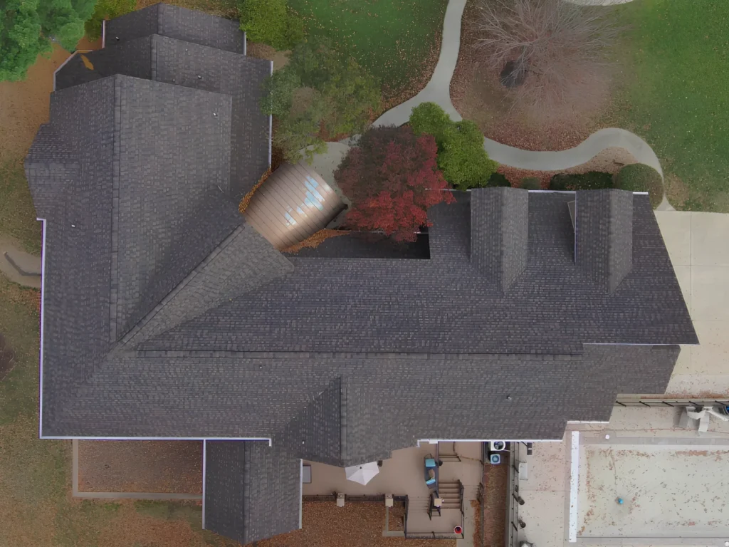 This image is showing an aerial view of a large residential property with a new dark gray architectural shingle roof installation, featuring multiple roof sections and beautiful landscaping in Lake Ozark.