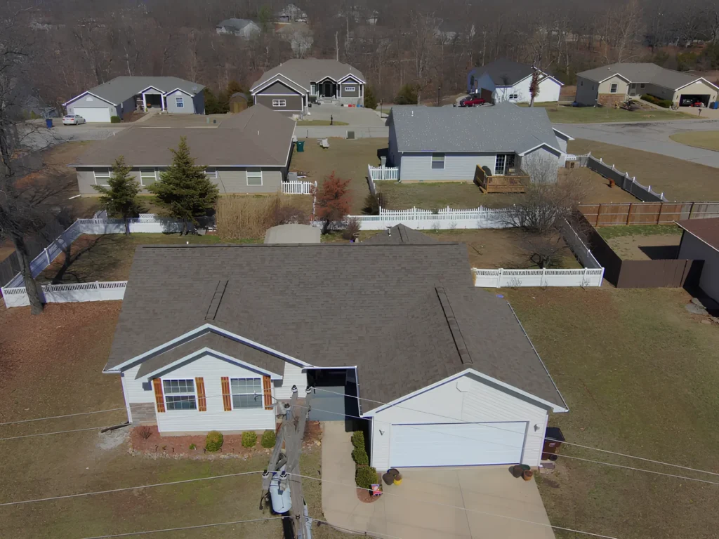 This image is showing a residential neighborhood with a newly installed brown shingle roof on a single-story white home with attached garage in the Lake of the Ozarks area.