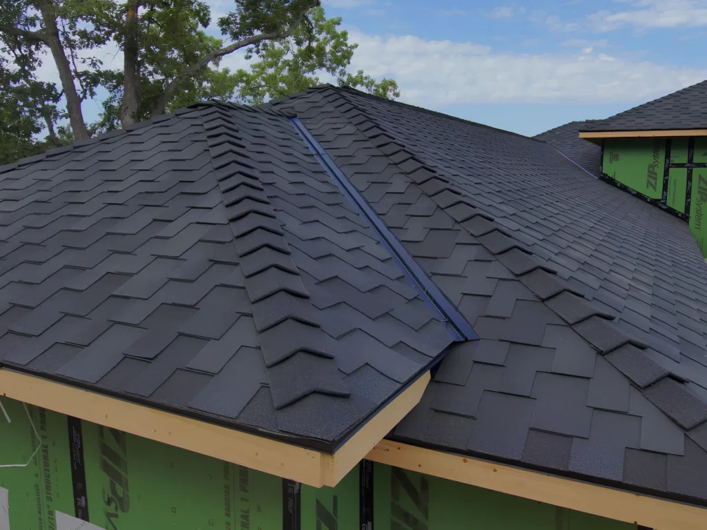This image is showing a close-up of premium black architectural shingles being installed on a new construction home with green weather barrier visible at the roof edge in Lake Ozark.