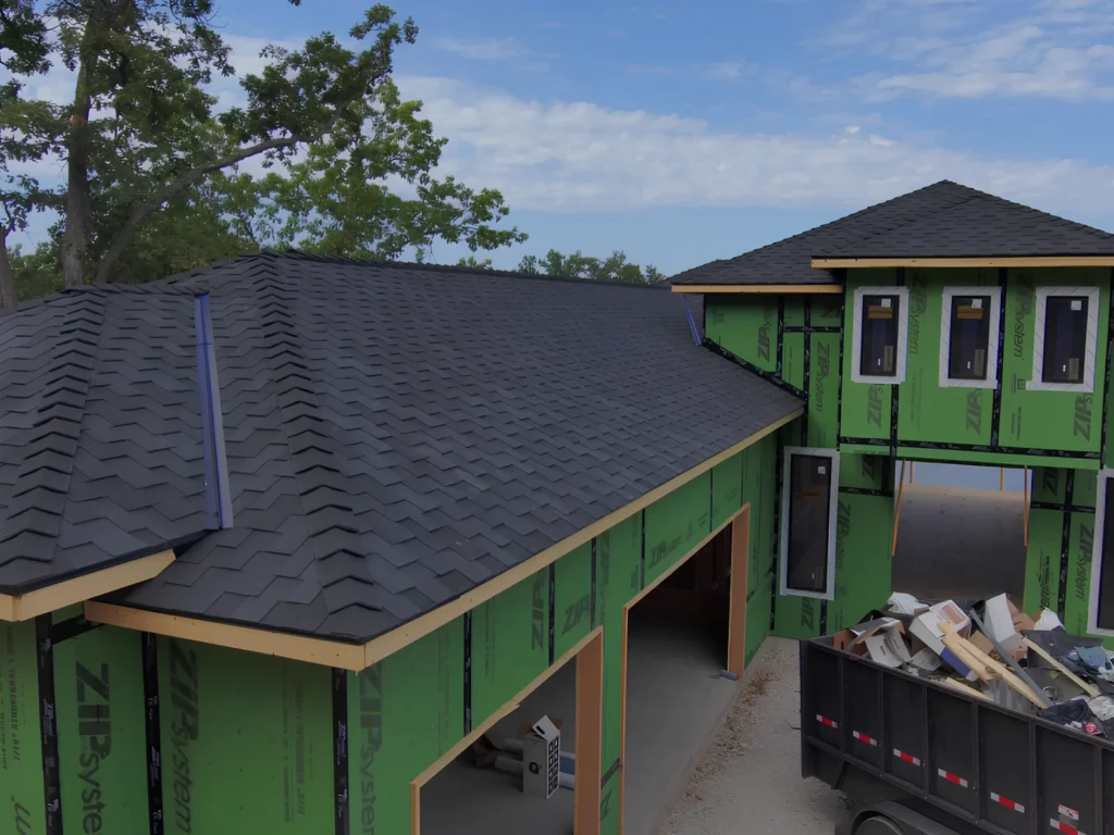 This image is showing a new construction home with black architectural shingles being installed on green ZIP system sheathing, highlighting custom home building services in Lake Ozark.