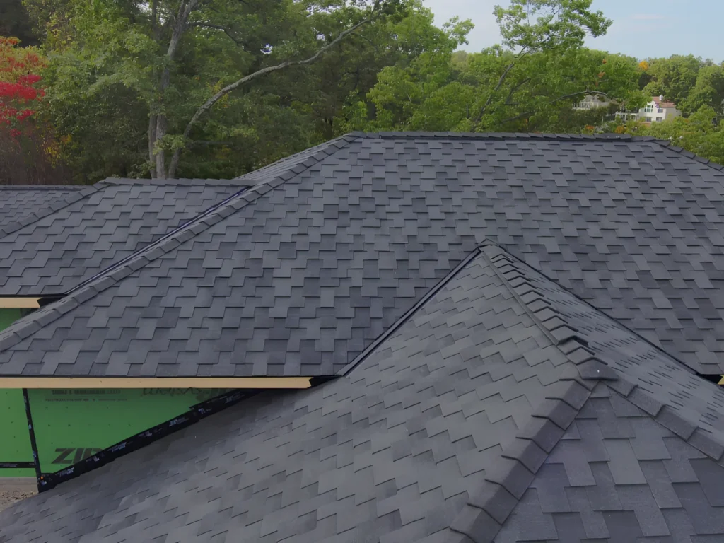This image is showing detailed architectural shingle installation on a new construction home in Lake Ozark, featuring precise valley work and dimensional gray shingles against green ZIP system sheathing.