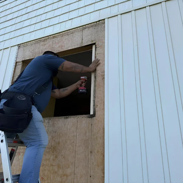 This image is showing a person using a power drill on a ladder during exterior wall framing for a building renovation.